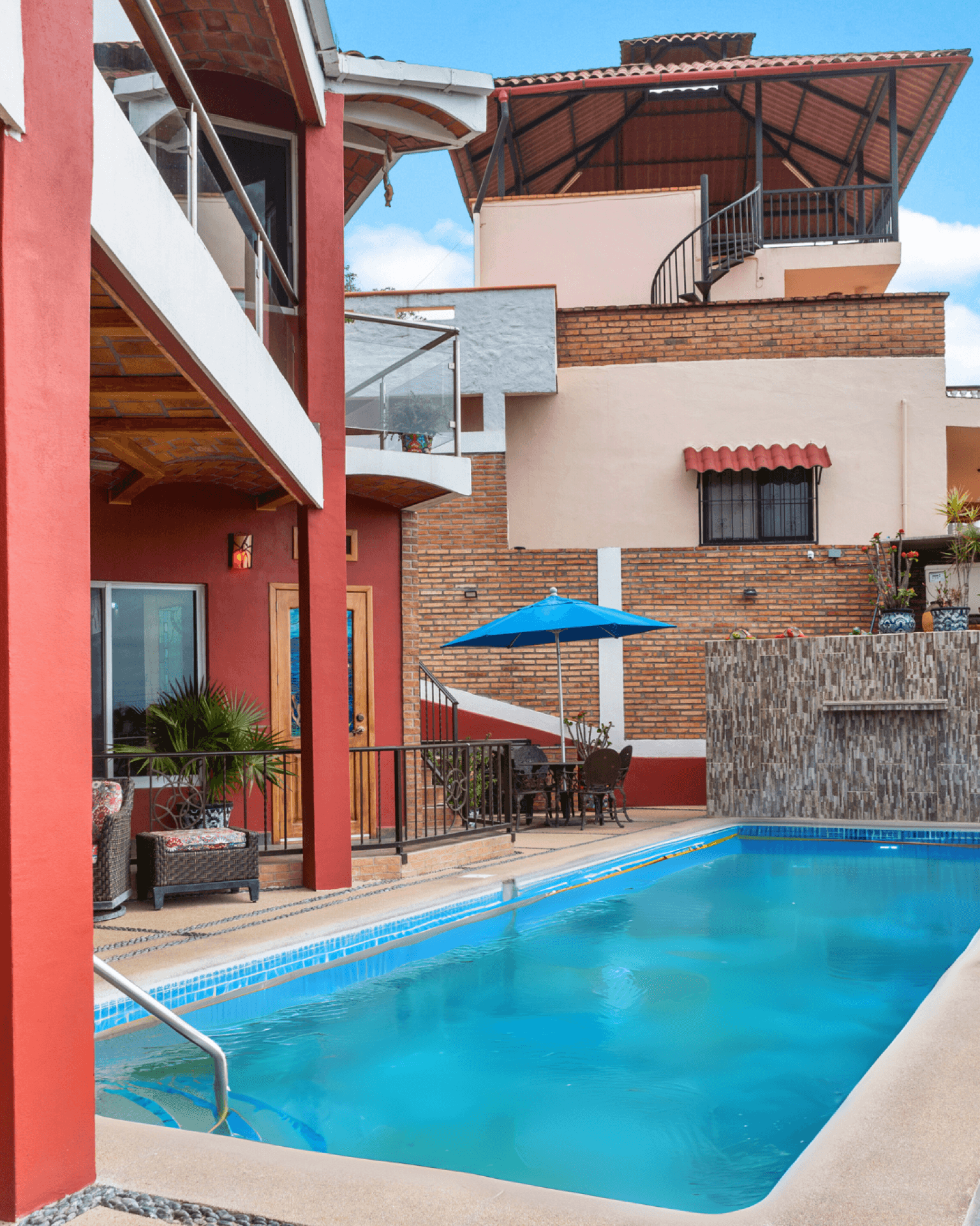 Heated pool with vibrant Mexican architecture and blue umbrella showing wider property context